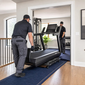 Professional delivery team moving a treadmill safely through a home doorway using protective blankets and a dolly